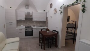 A compact kitchen with white cabinets, a dining table, and chairs. There is a small oven and a sink. - I Cappuccini B&B (Sorso)