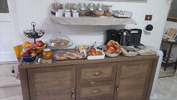 A buffet setup with various food items and condiments on a wooden cabinet. - I Cappuccini B&B (Sorso)