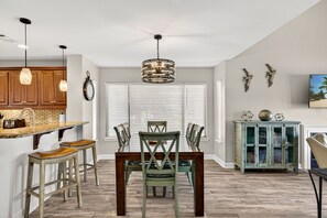 A dining area with a wooden table, four chairs, a chandelier, and a cabinet with decorative items. - Golf Cart ~ End Unit with Loft ~ Master Balcony (Miramar Beach)