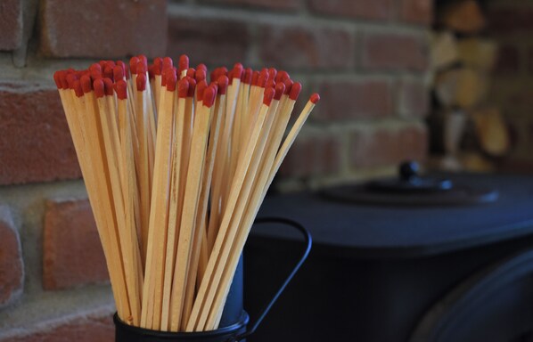 A black metal cup filled with wooden matches with red tips, placed on a surface with a brick wall in the background.