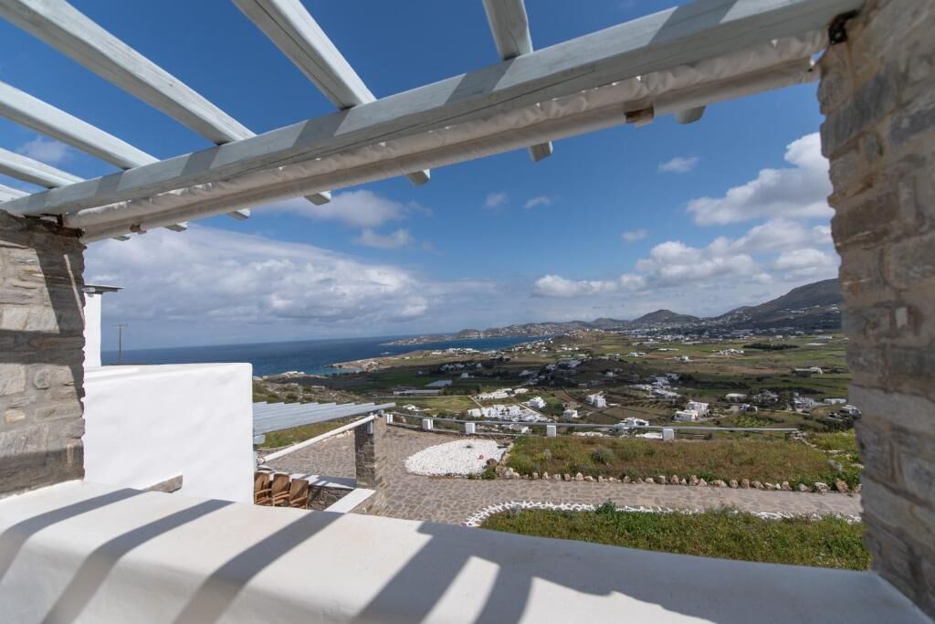 A view from a balcony with a pergola, overlooking a coastal landscape with houses and hills.