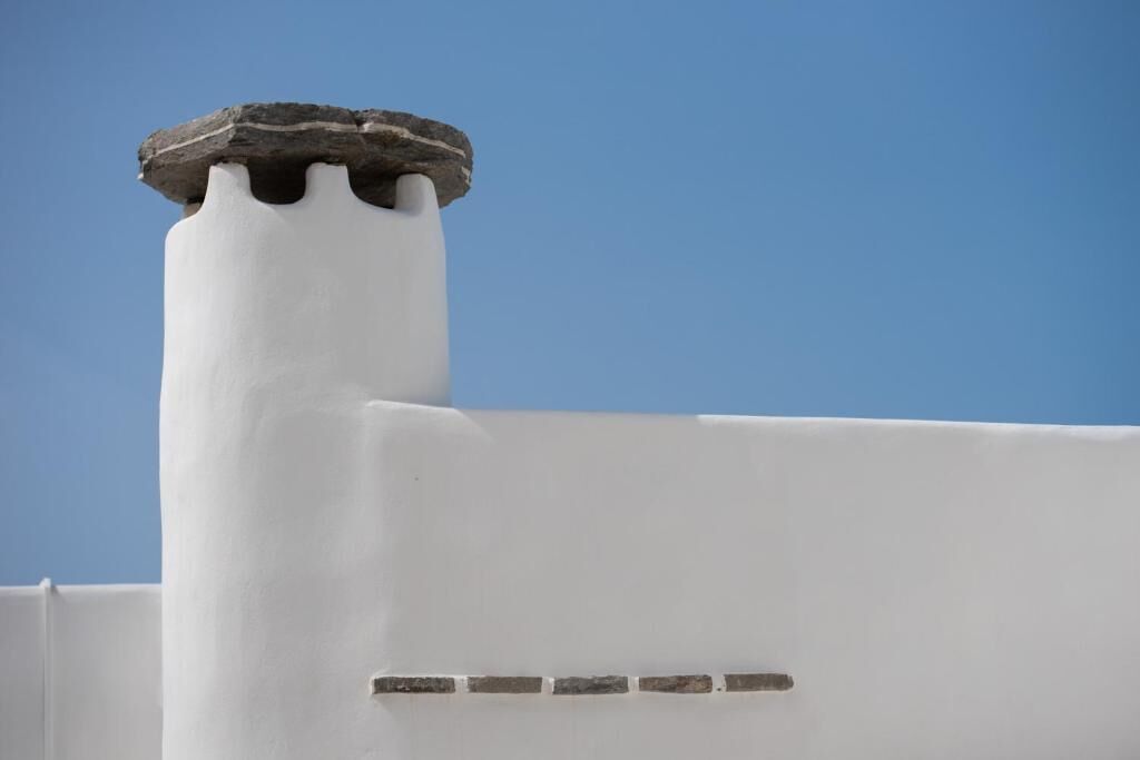 A white chimney with a stone cap against a clear blue sky.