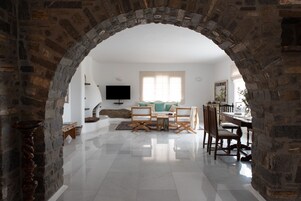 A living room with a stone archway, a sofa, a TV, and a dining area with chairs and a table.