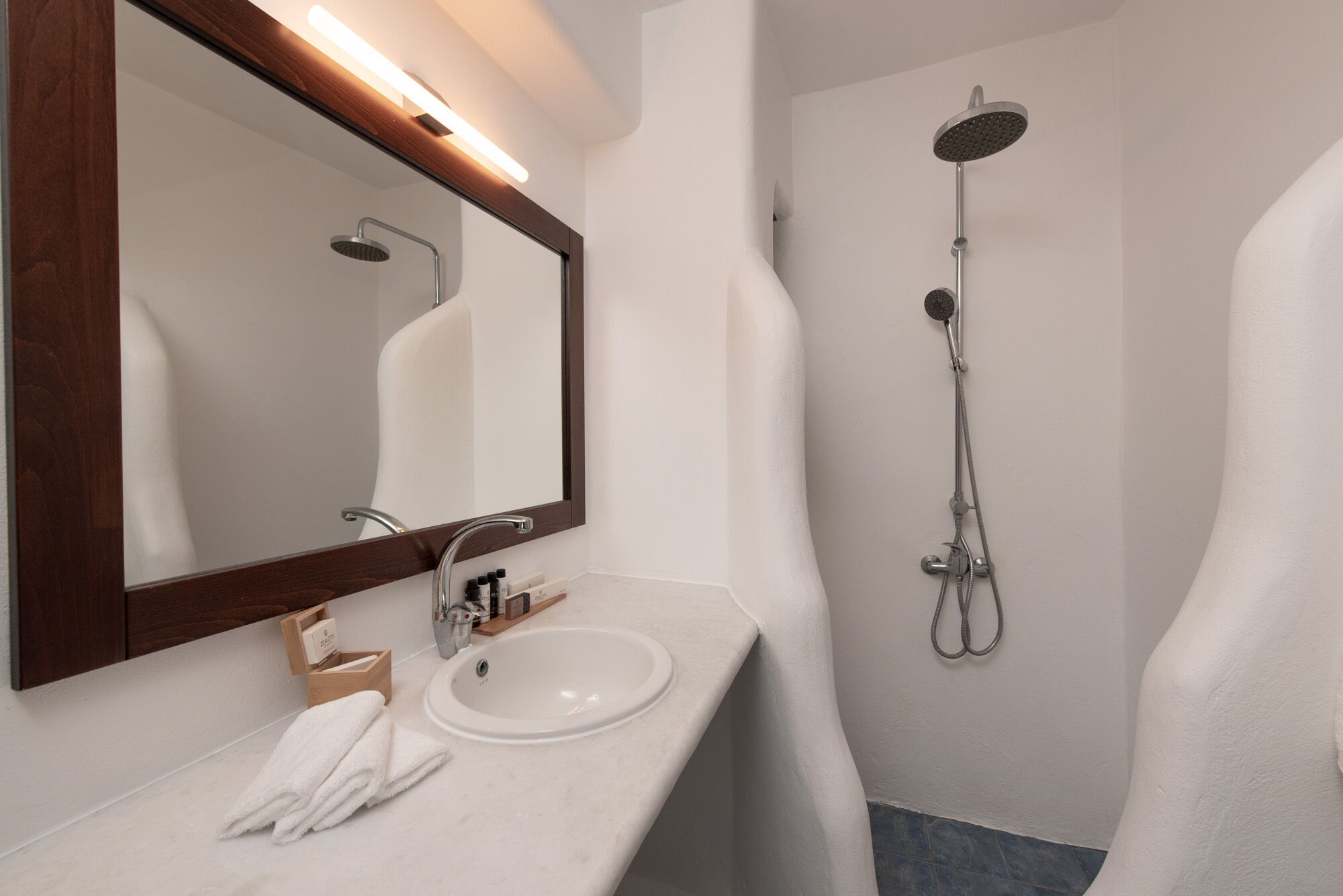 Un ba ño moderno con un lavabo blanco, un espejo grande y una ducha con cabezal de ducha manual.