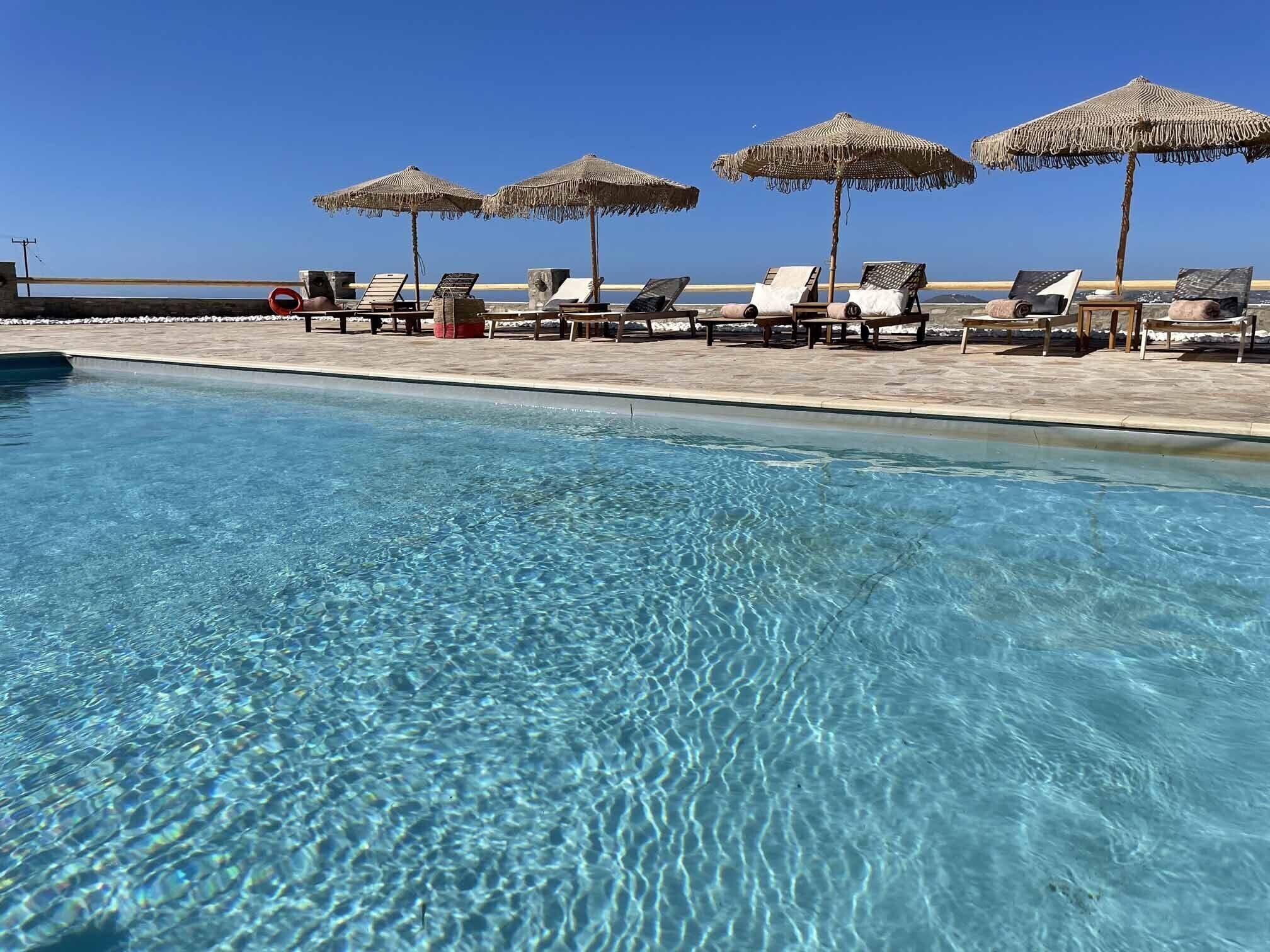 A clear swimming pool with lounge chairs and thatched umbrellas.