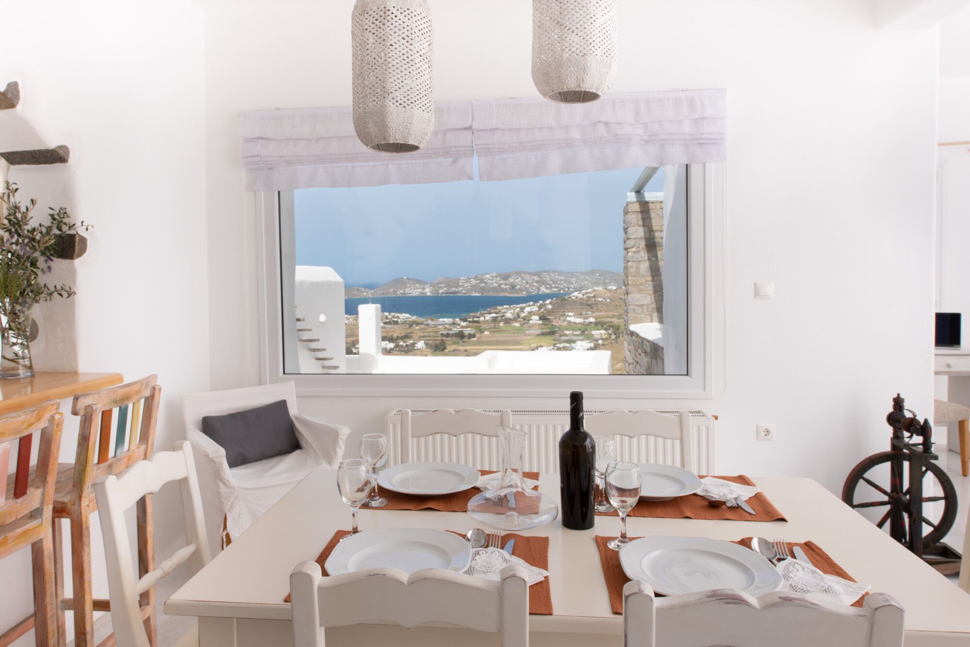 Un coin repas avec une table dressée pour quatre personnes, une vue sur la mer et les bâtiments, et un vélo posé dans un coin.