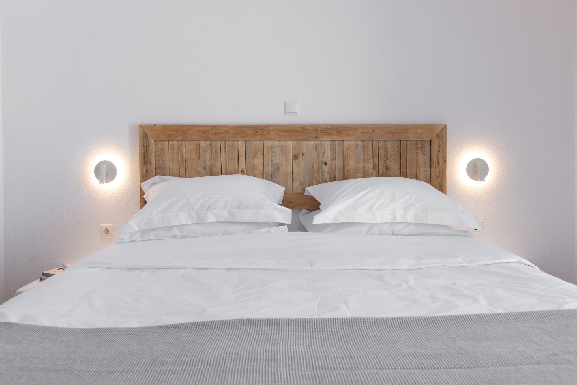 A bed with a wooden headboard, two white pillows, and two wall-mounted light fixtures.