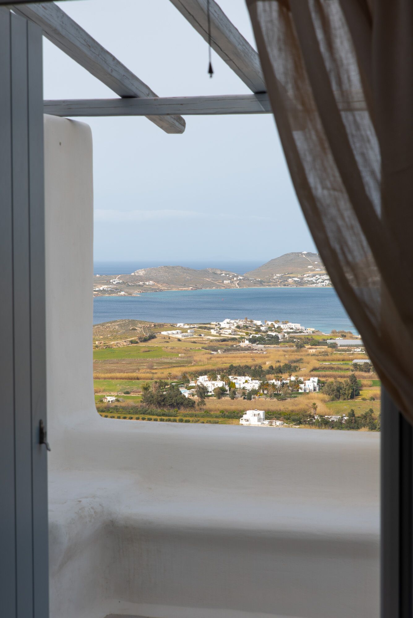 A view from a window overlooking a coastal landscape with buildings and a mountain in the distance.
