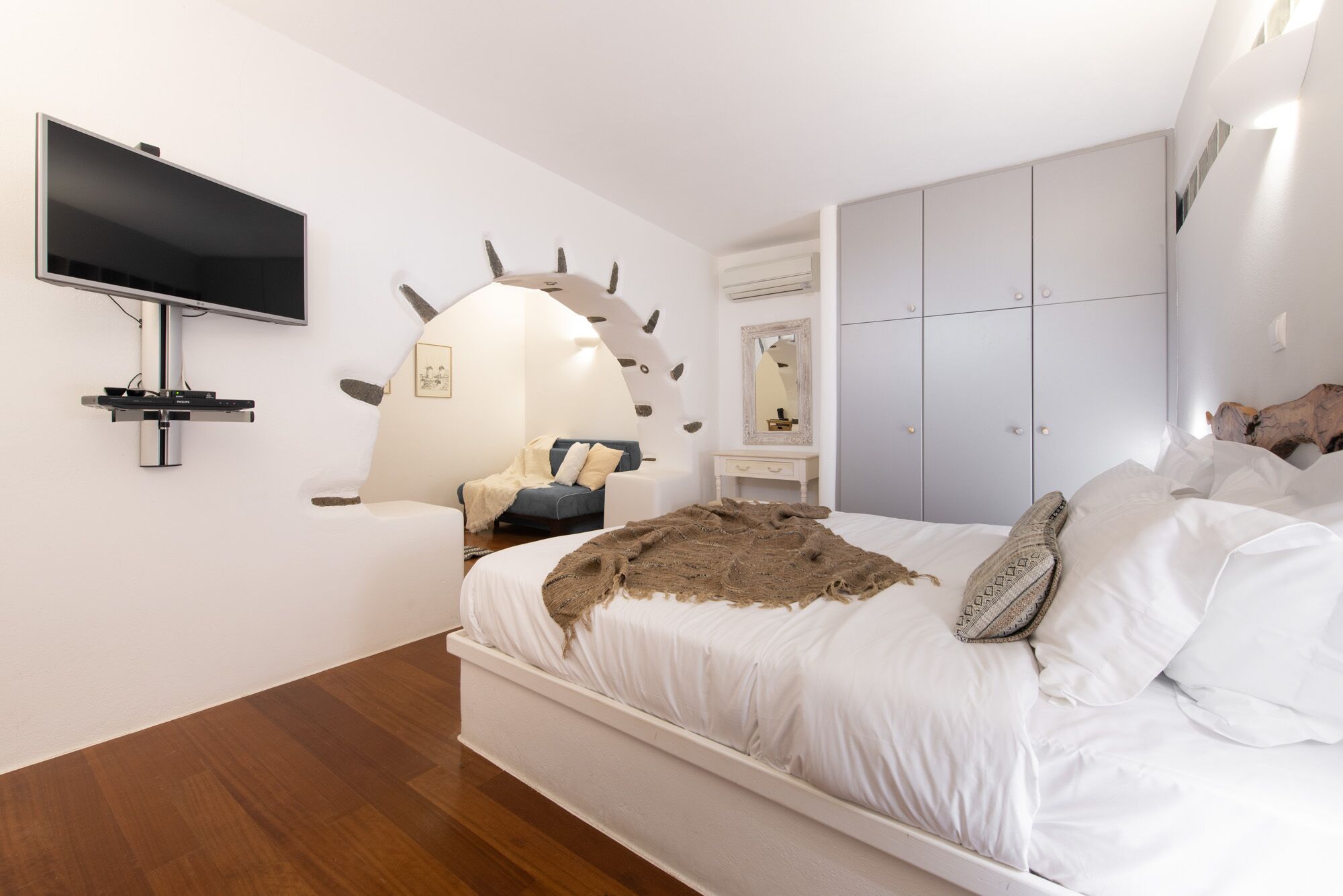 A modern bedroom with a large bed, a mounted TV, a unique wall sculpture, a dresser, and a wardrobe.