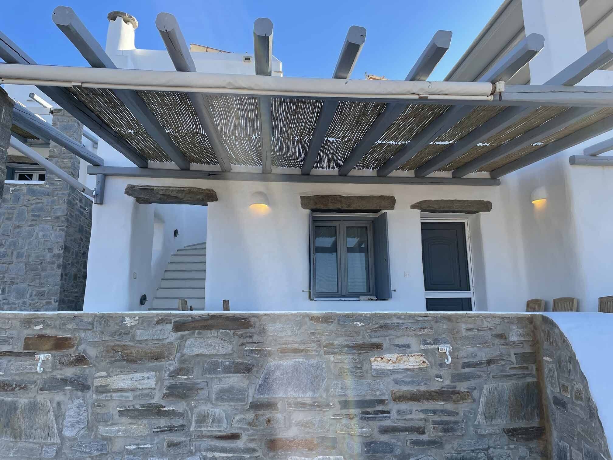 En bygning med en stenvæg, en træpergola og en trappe, der fører op til en etage.