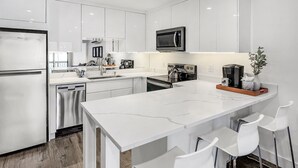 A modern kitchen with white cabinetry, stainless steel appliances, and a central island with bar stools.