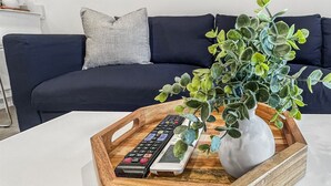 A living room with a white coffee table holding a tray with a remote control, a white vase with green plants, and a framed ski poster.