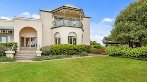 A two-story house with a balcony, a well-maintained lawn, and a variety of shrubs and trees.