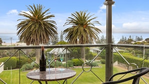 A balcony with a view of the sea, two palm trees, and a bottle of champagne on a table.