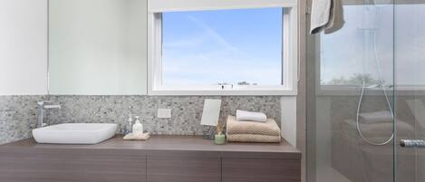 A modern bathroom with a large window, a vessel sink, and a shower area.
