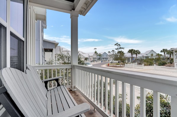 A balcony with a white chair, overlooking a residential street with houses and a clear sky.