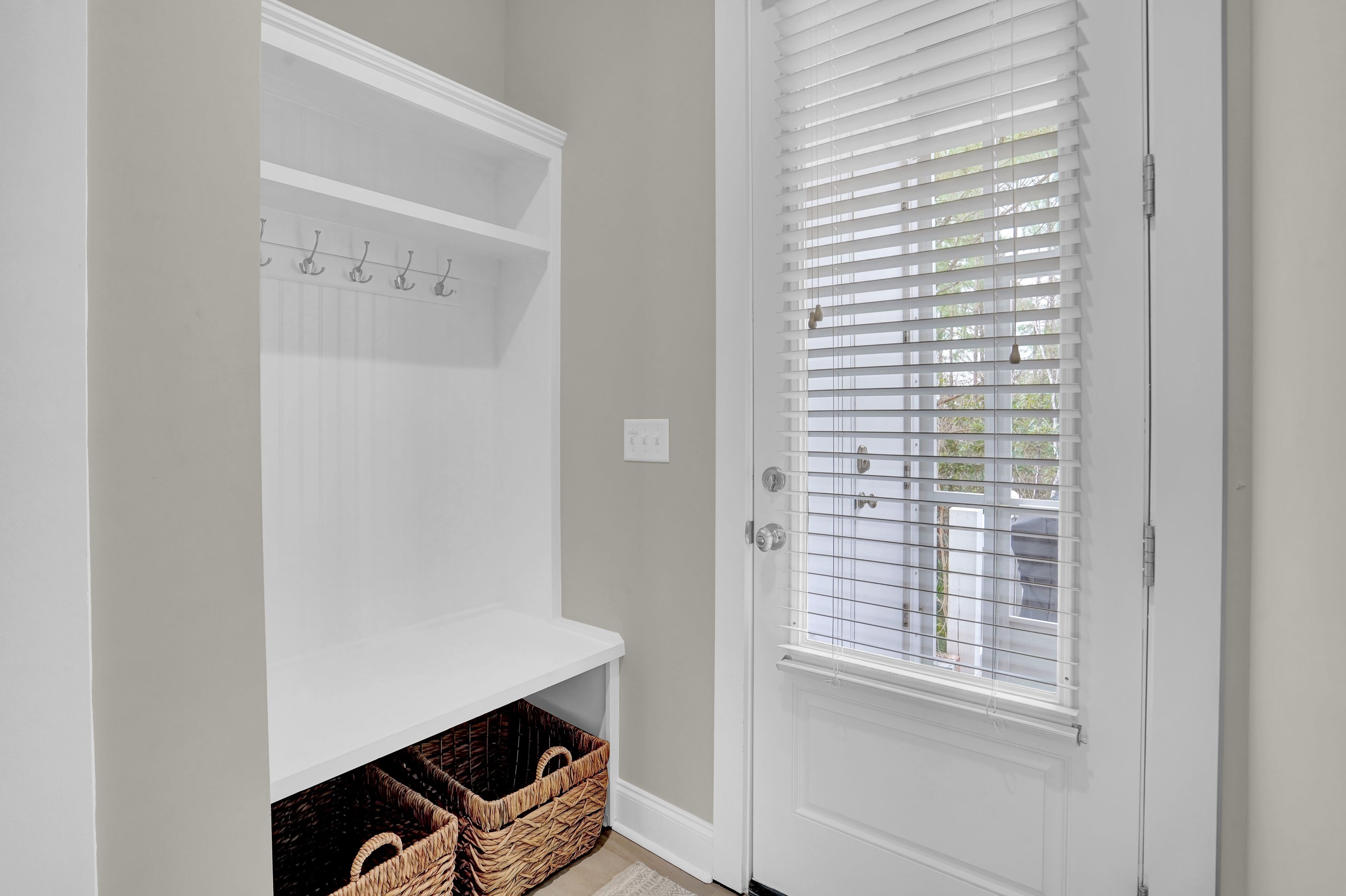 A hallway with a white door, a coat rack, and wicker baskets.