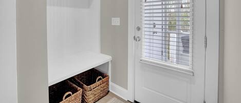 A hallway with a white door, a coat rack, and wicker baskets.
