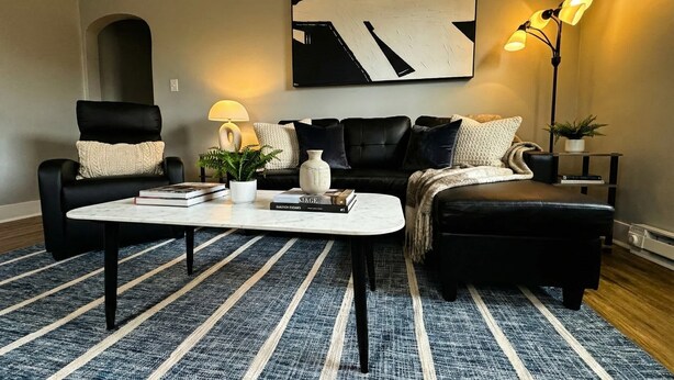 A modern living room with a black leather sofa, a coffee table, and a large abstract painting on the wall. - Newly Renovated Apt with King Bed (Wilmington)