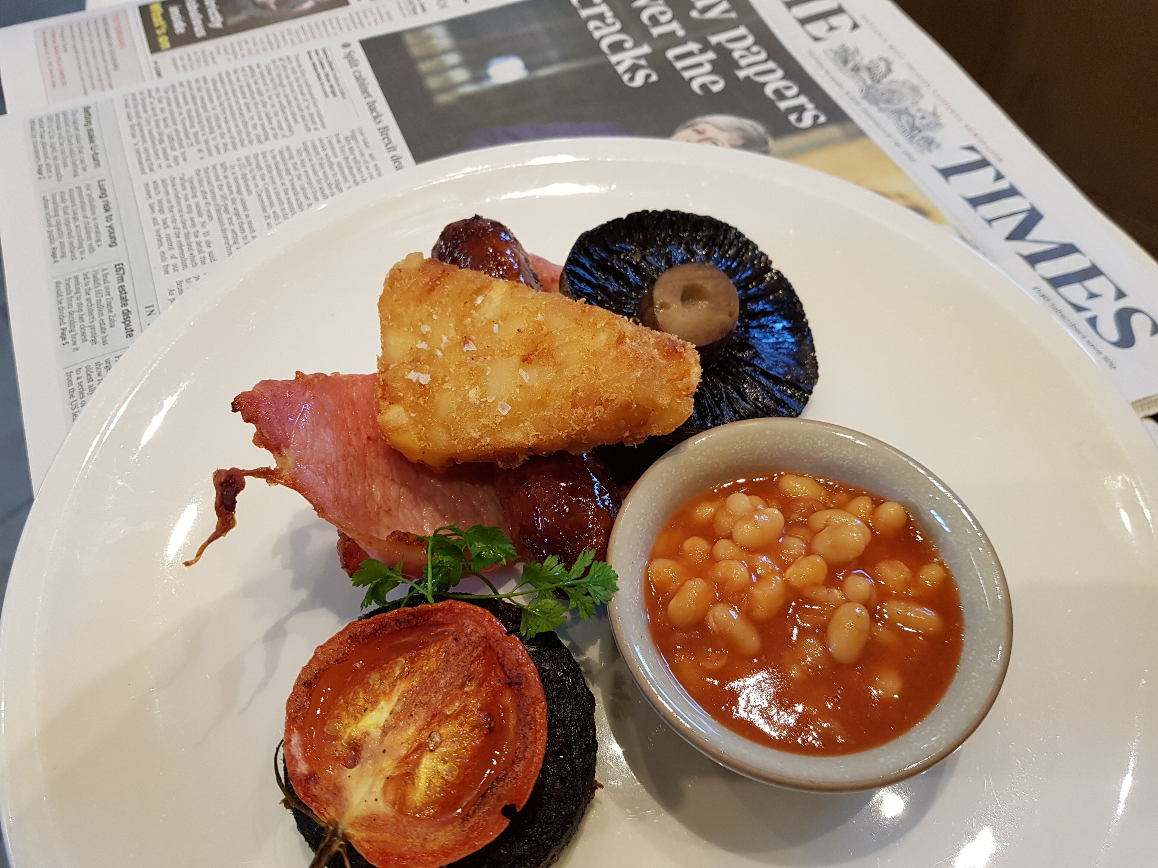 A plate with various foods including bacon, mushrooms, a fried item, and a bowl of beans.