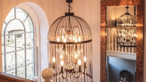 A staircase with a wooden handrail and white balusters, leading to a landing with a large arched window and a chandelier with multiple bulbs. - The Saddle Room Restaurant (Leyburn)