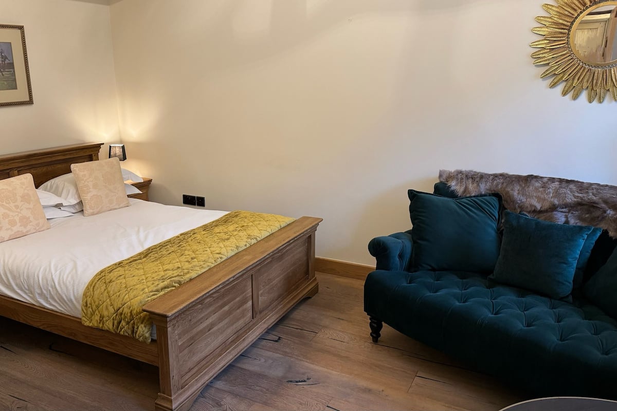 Un dormitorio con una cama de madera, un sofá verde, un cuadro en la pared y un espejo con forma de sol.