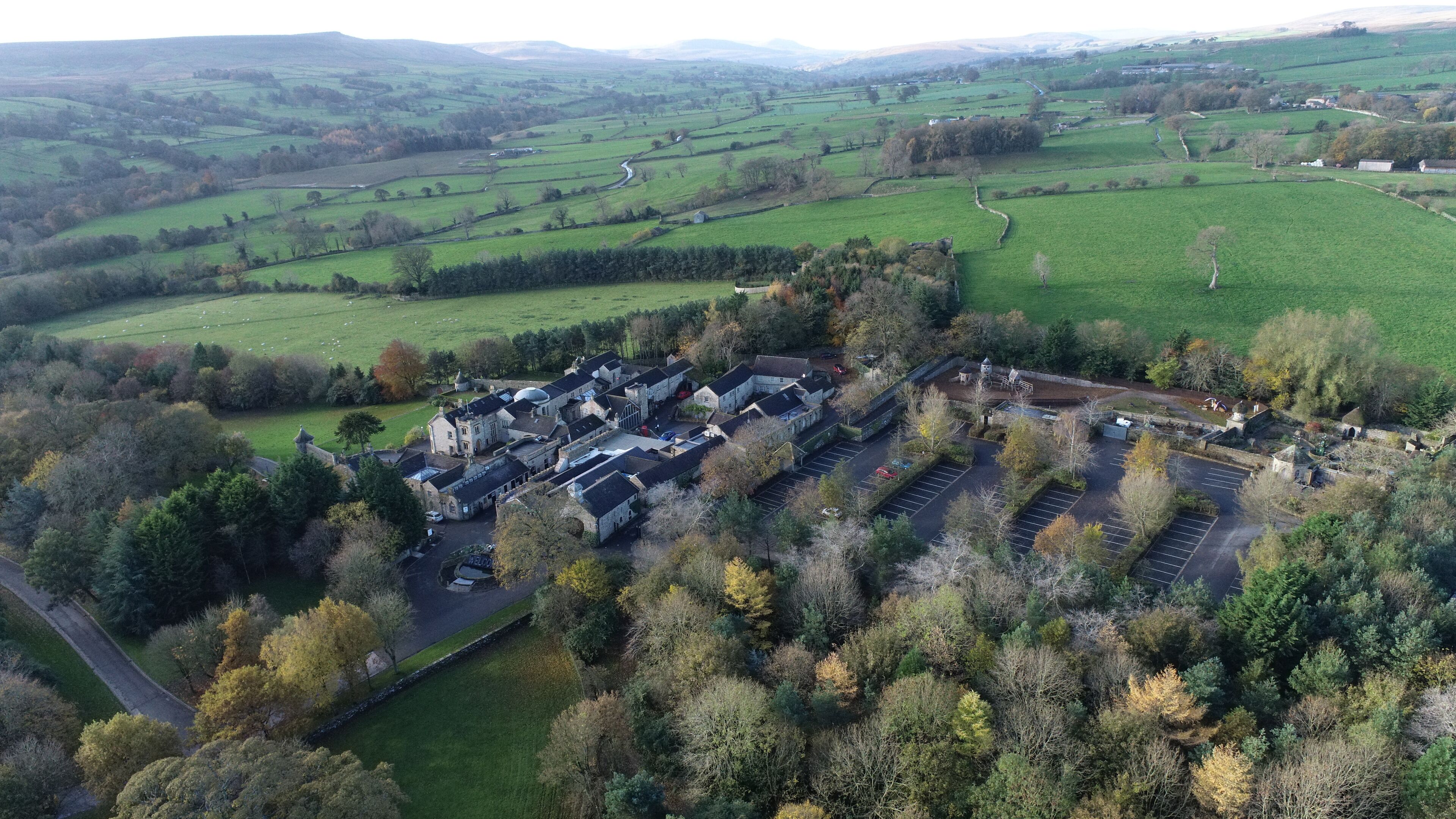 An aerial view of a rural estate with multiple buildings, a large parking area, and surrounding green fields.