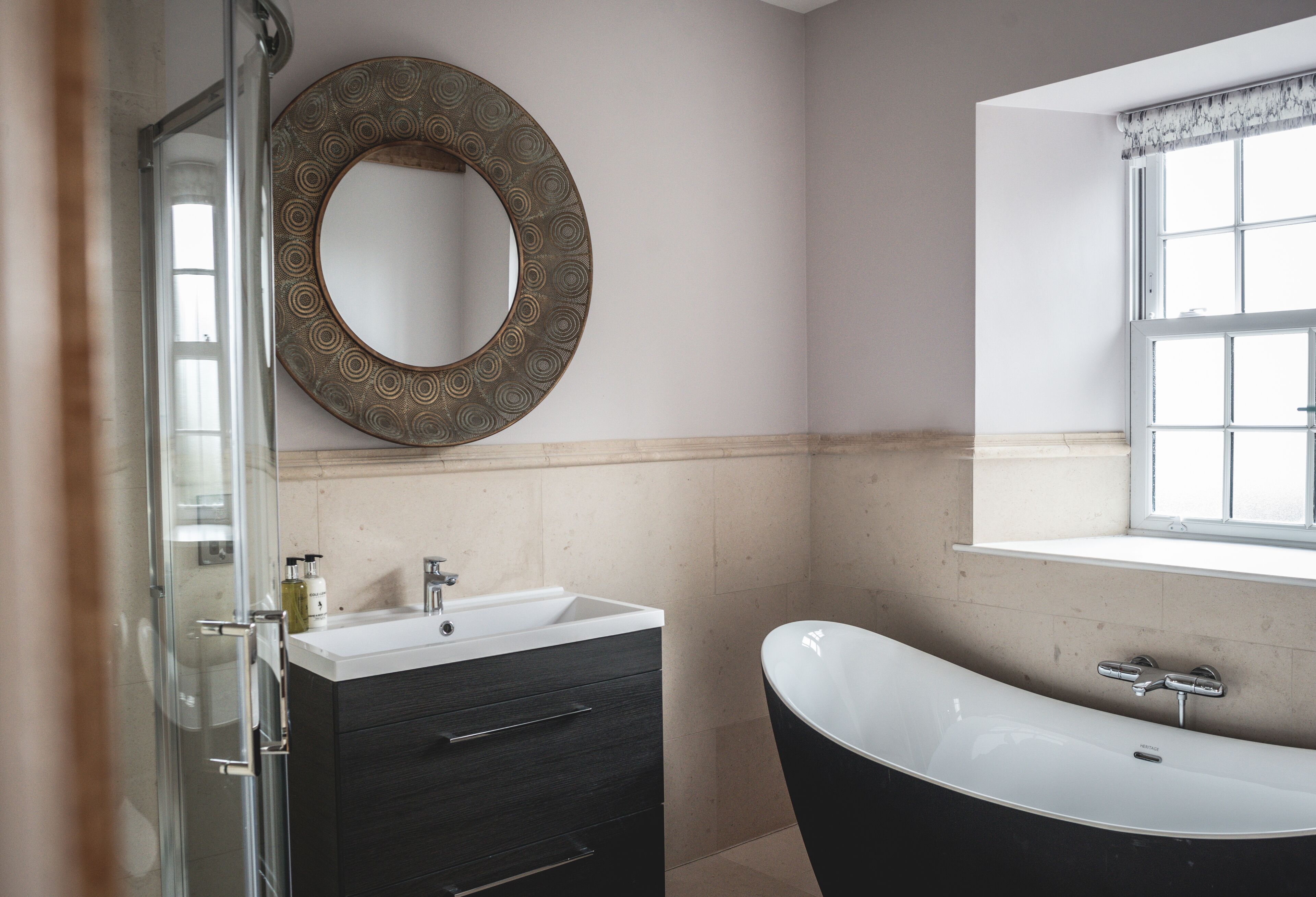 A bathroom with a freestanding bathtub, a round mirror, and a glass shower enclosure.