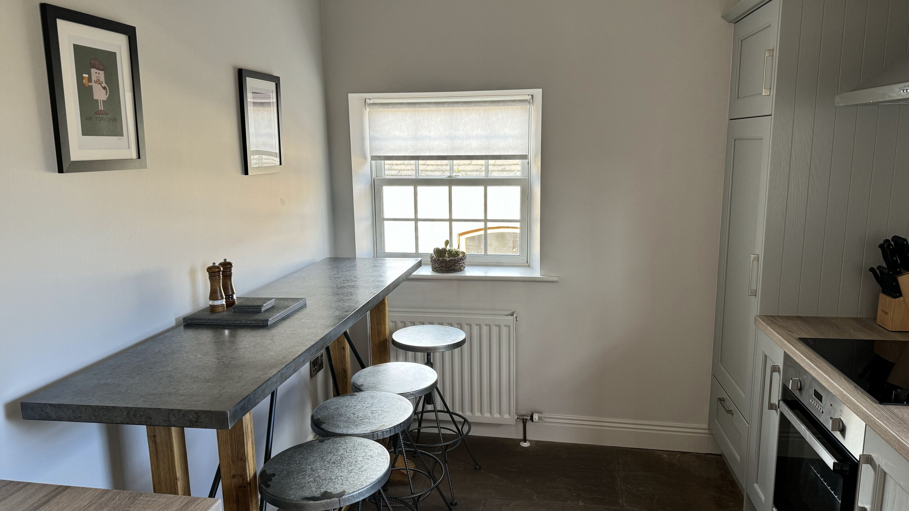 A kitchen with a long counter, bar stools, a window with blinds, and a white refrigerator.