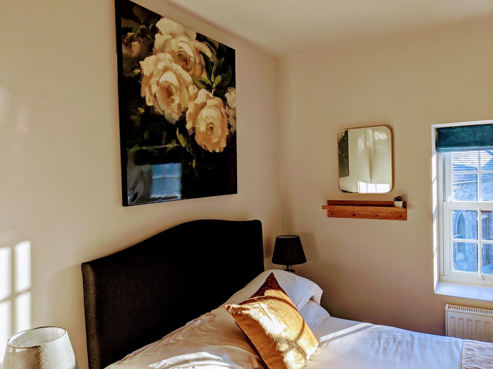 Un dormitorio con cama, un cuadro de flores, una lámpara de noche, un espejo y una ventana con vistas.