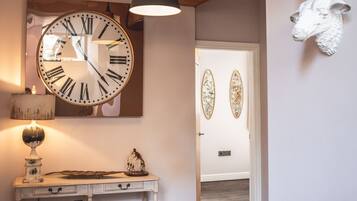 A hallway with a large wall clock, a wooden ceiling beam, and decorative sheep heads on the wall.