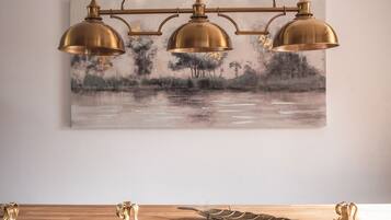 A dining area with a wooden table, three gold pendant lights, and a landscape painting on the wall.