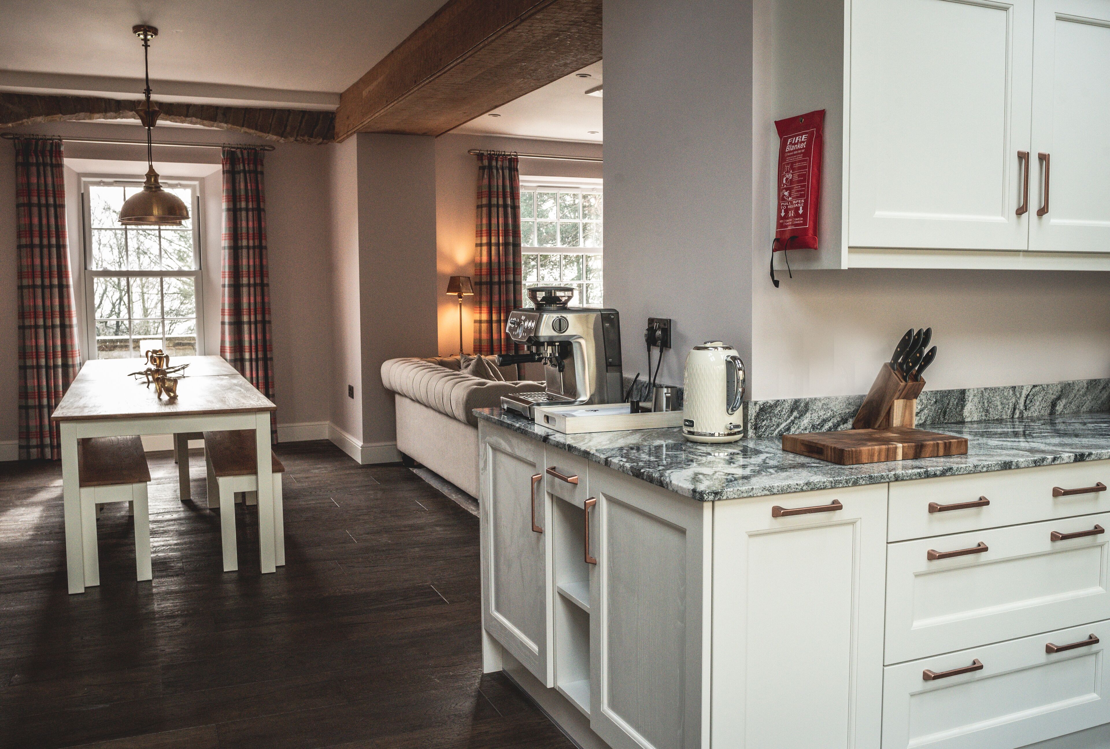 Una cocina moderna con armarios blancos, encimera de mármol y comedor con mesa y sillas.