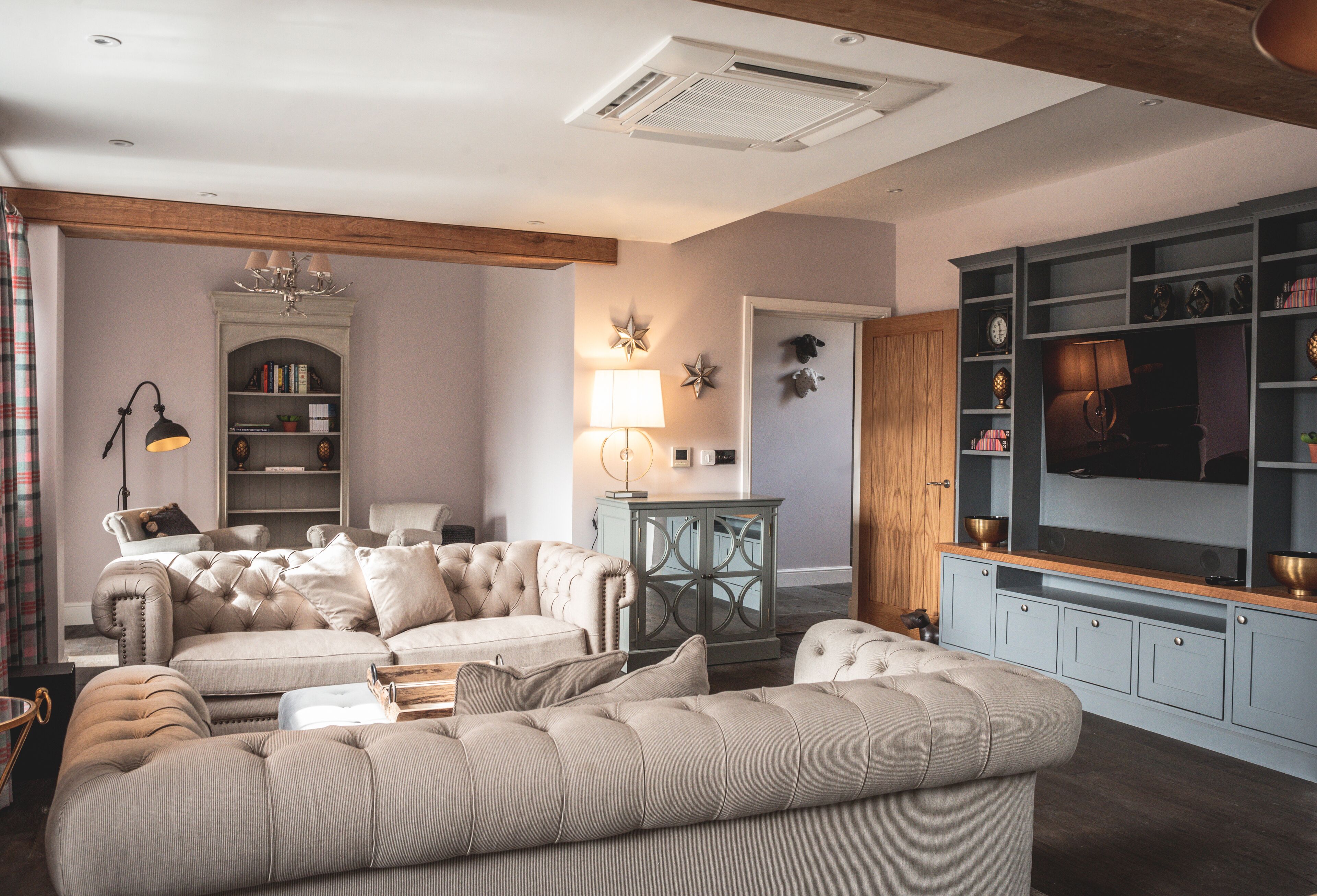 A living room with a large sectional sofa, a wooden ceiling, and built-in shelving with decorative items.