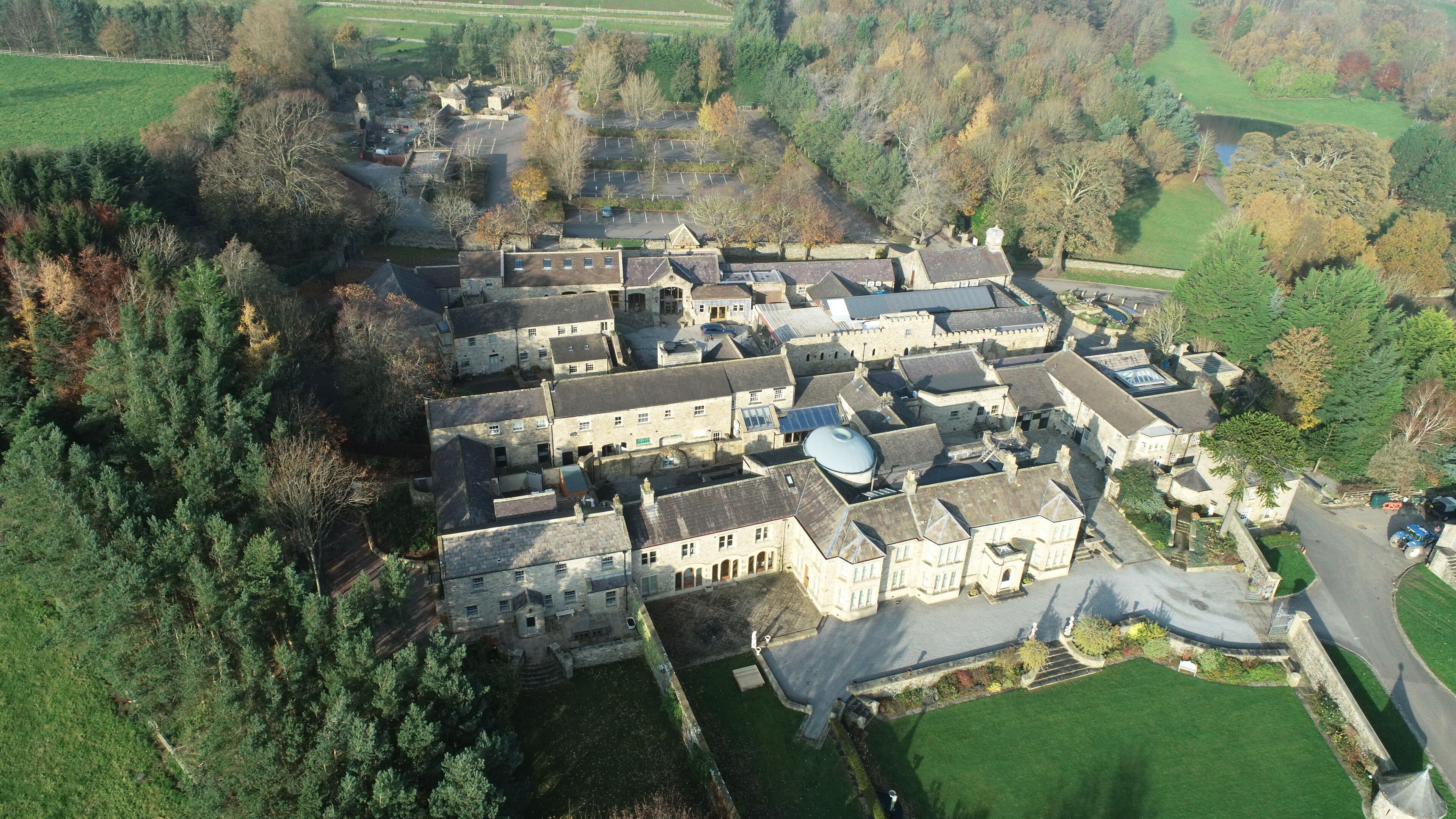 An aerial view of a historic building complex with multiple structures, including a central courtyard and surrounding gardens.