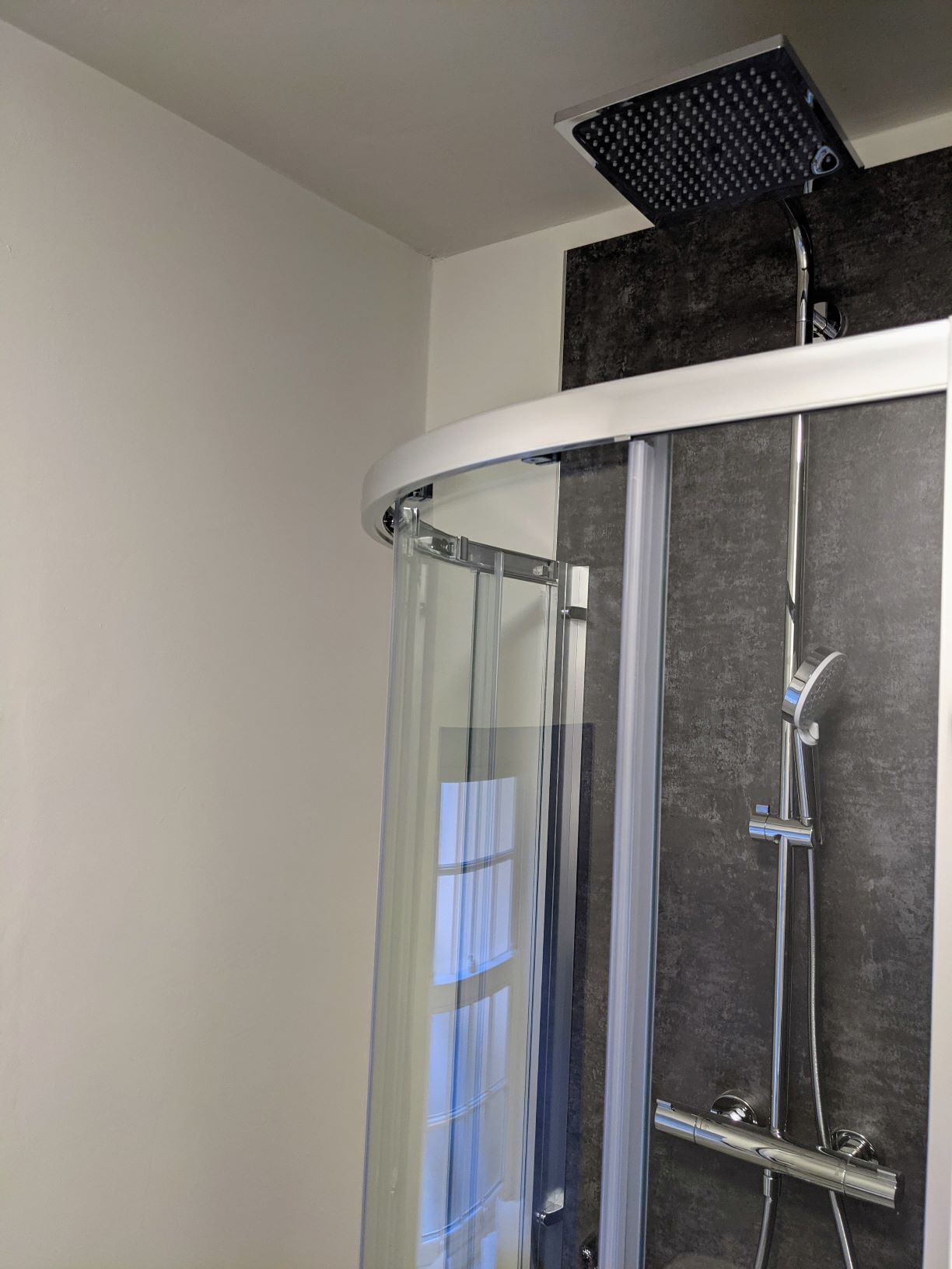 A shower with a glass door, a handheld showerhead, and a wall-mounted faucet.