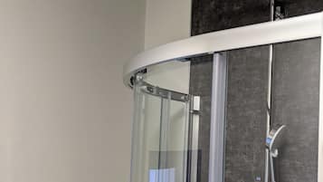 Eine Dusche mit Glastür, Handbrause und Wandarmatur.