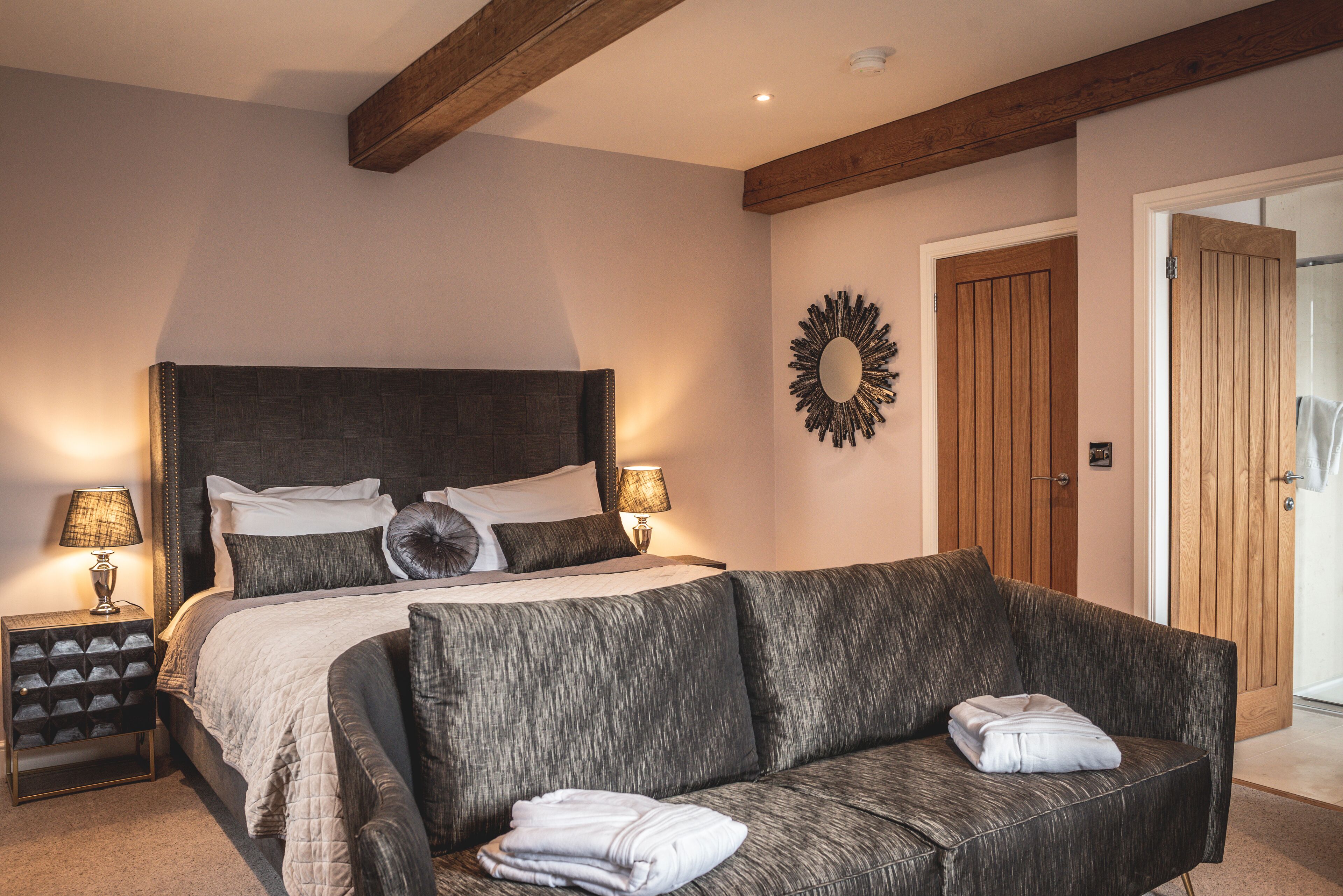 A bedroom with a bed, two bedside tables with lamps, a sofa, and a wooden door.