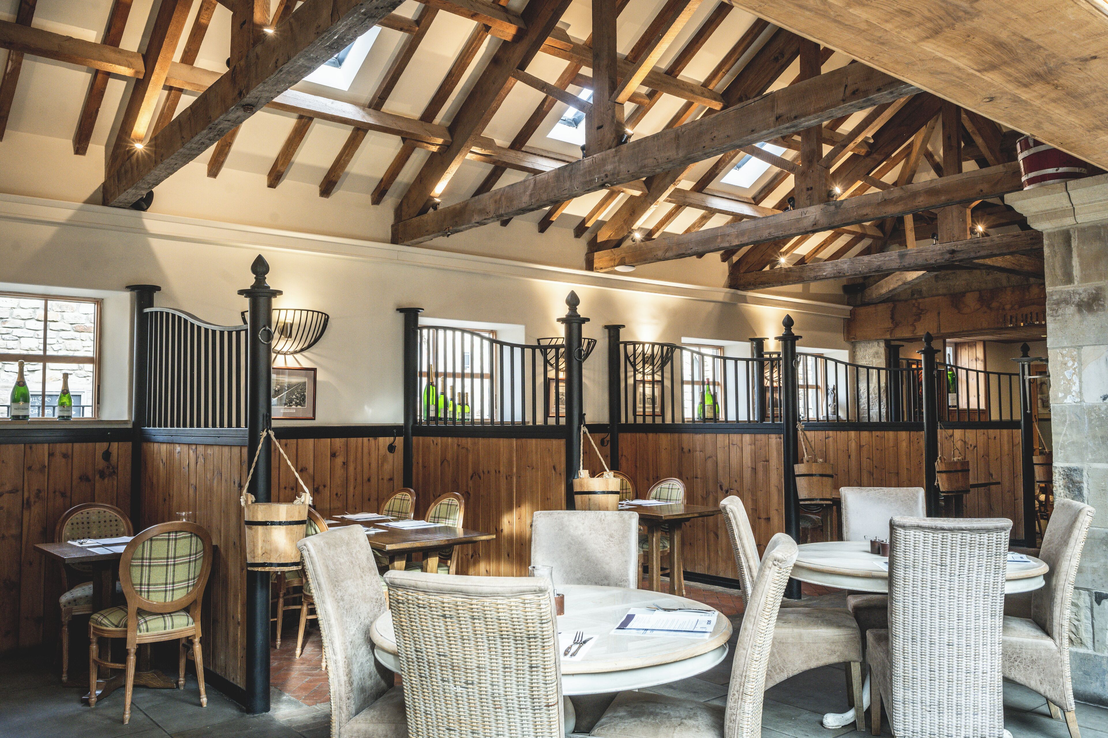 A restaurant with wooden beams, wicker chairs, and tables.