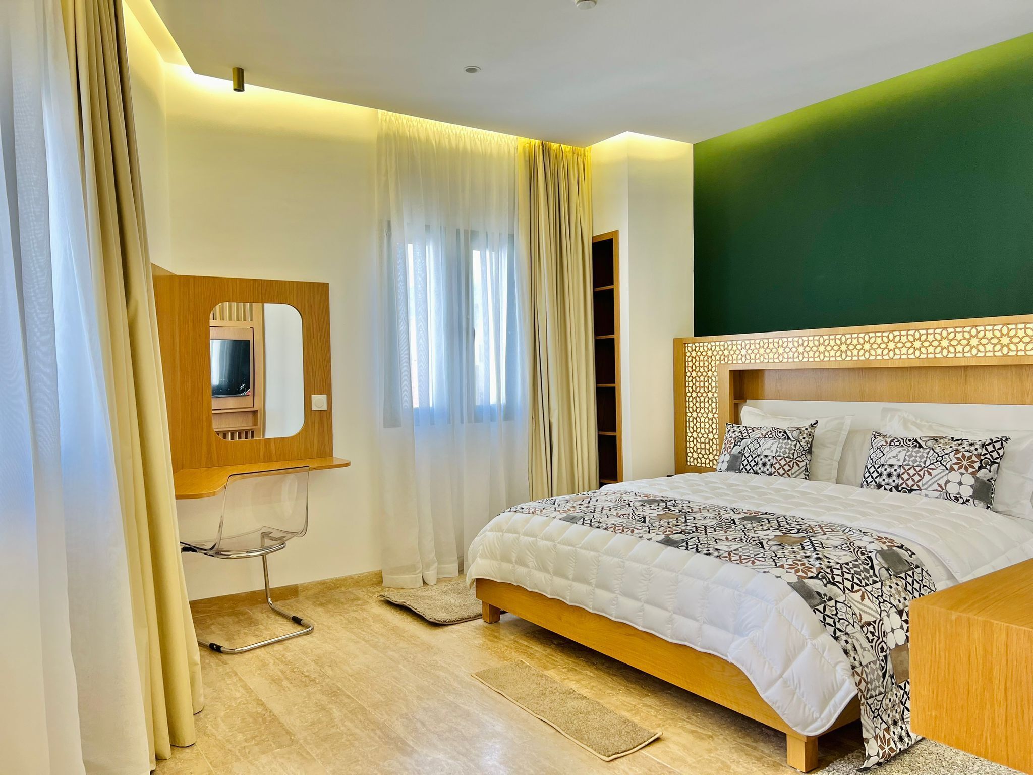 Un dormitorio con cama, mesita de noche, espejo y ventana con cortinas.