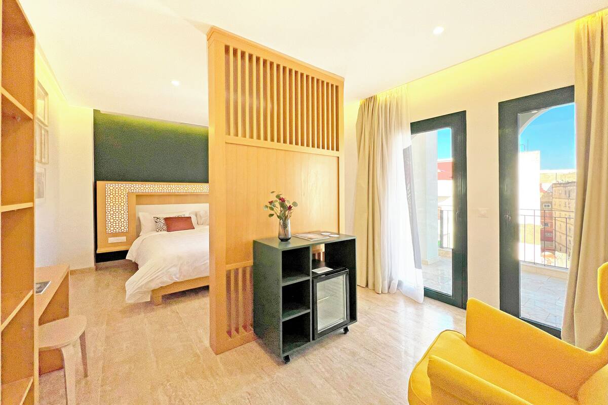 A hotel room with a bed, a desk, a chair, a TV, and a window with a view.