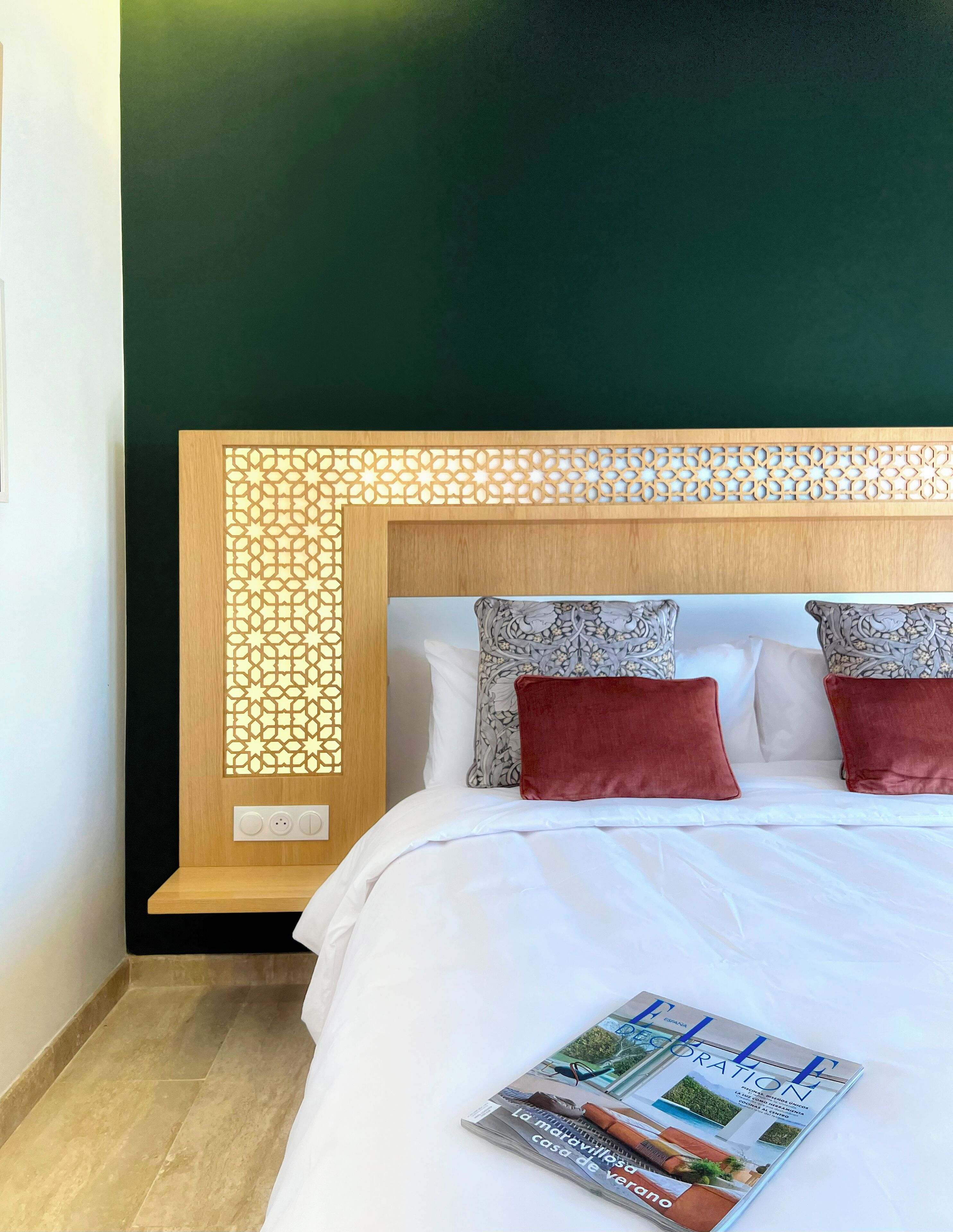 A neatly made bed with a magazine, a decorative headboard, and a green wall.