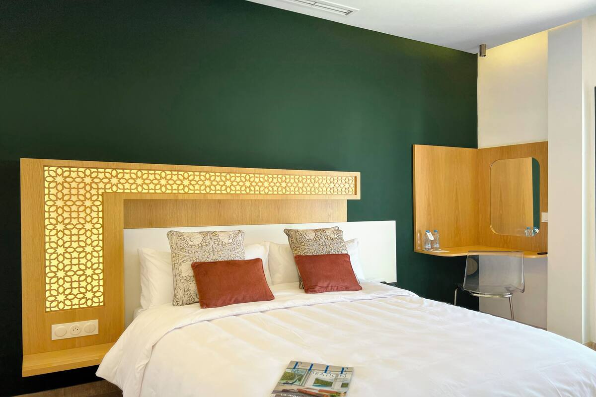 A hotel room with a bed, a wooden headboard with a geometric pattern, two pillows with a floral design, and a magazine on the bed.