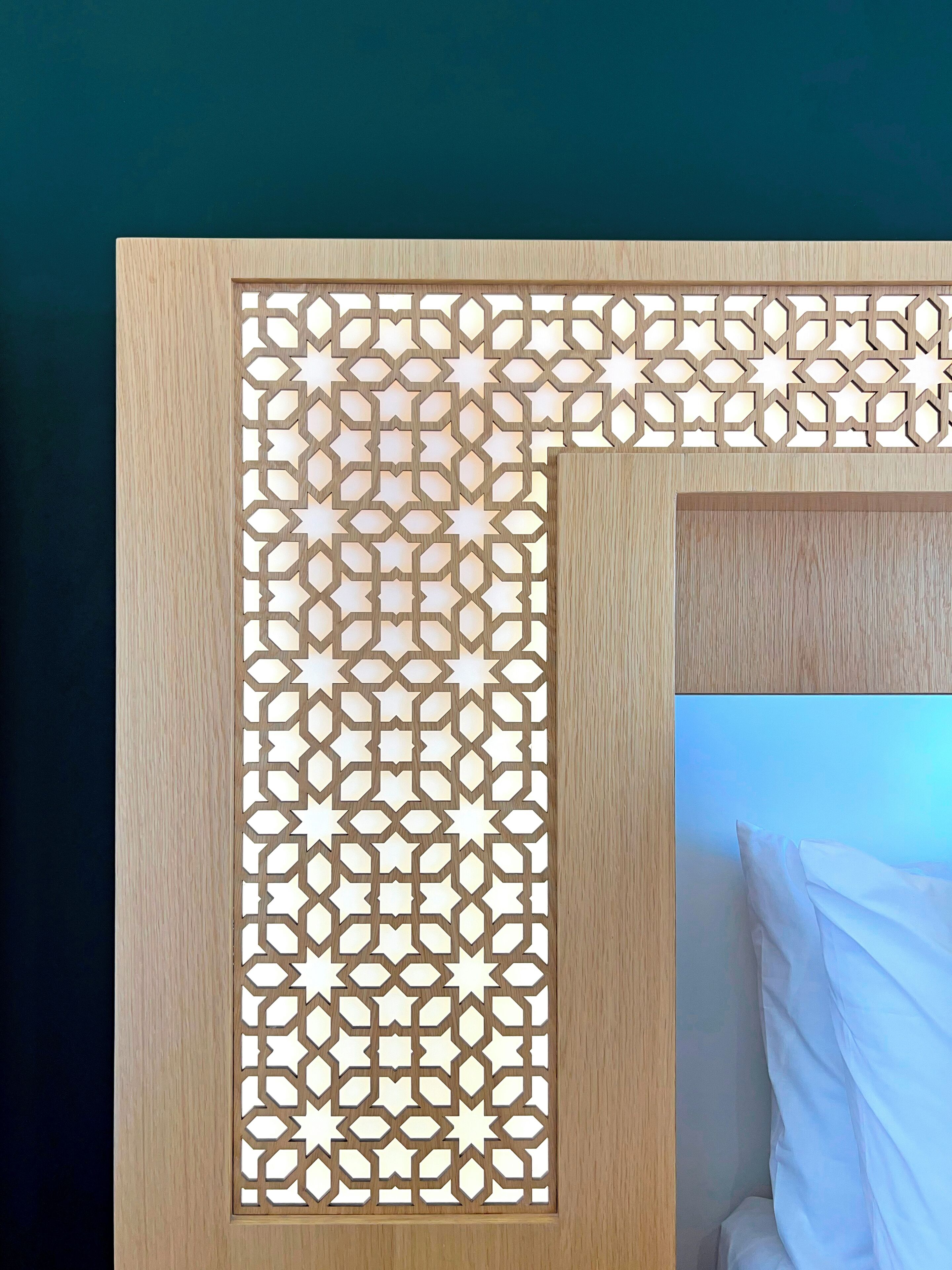 Cabecera de madera con un diseño geométrico y un almohadón en la cama.