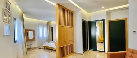 A modern hotel room with a bed, a wooden partition, a sofa, and a bathroom visible through an open door.