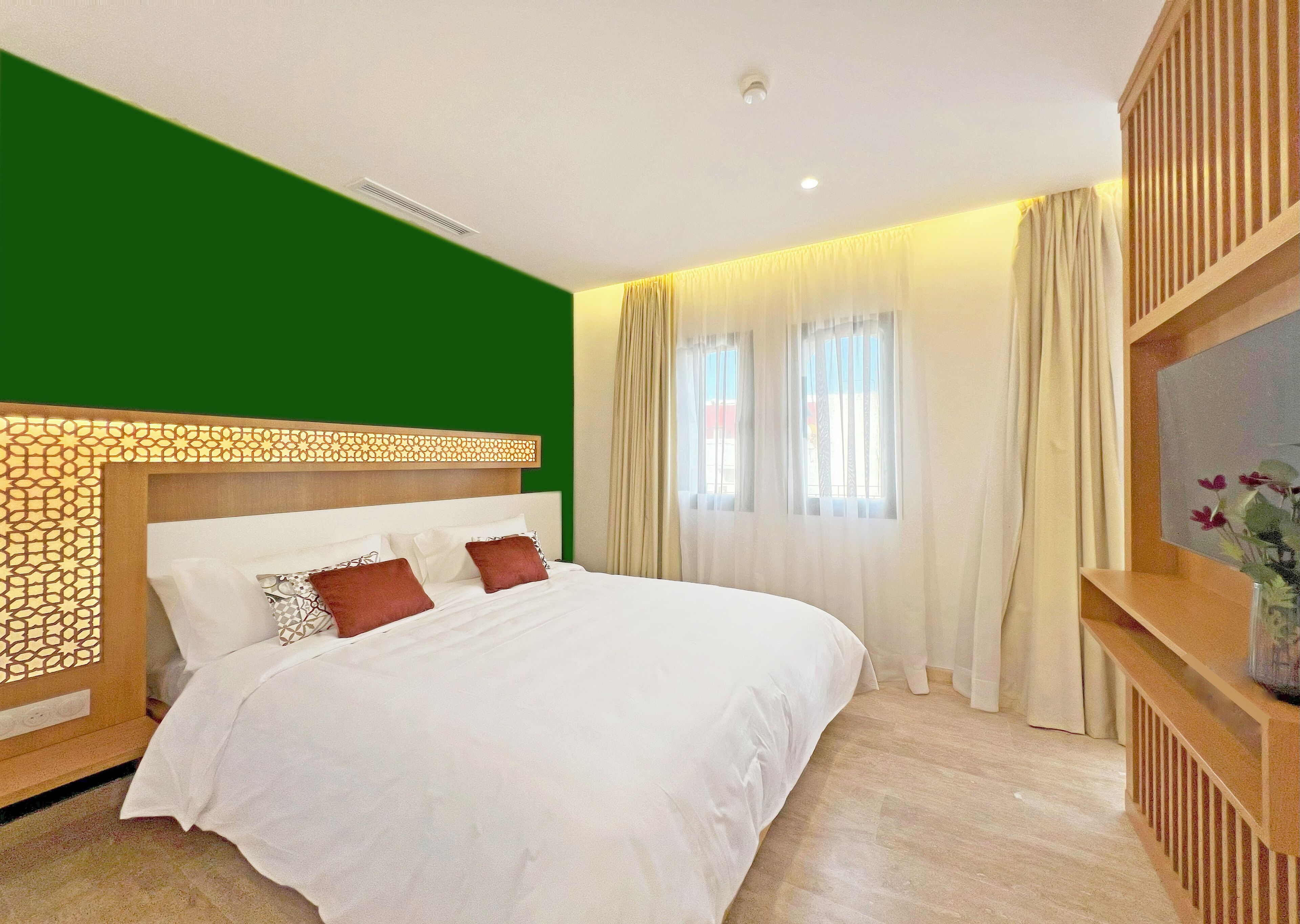 Habitació d'hotel amb un llit gran, una paret d'accent verd, un capçal de llit de fusta i una televisió sobre un suport de fusta.