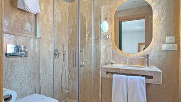 Un baño moderno con ducha de vidrio, inodoro, lavamanos con espejo y perchero para toallas.
