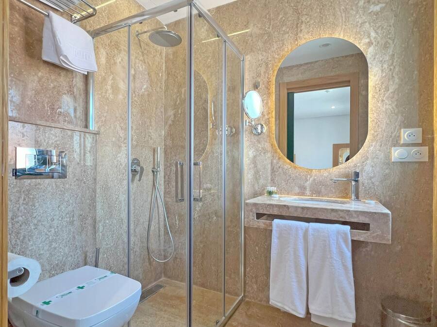 Un baño moderno con ducha de vidrio, inodoro, lavamanos con espejo y perchero para toallas.
