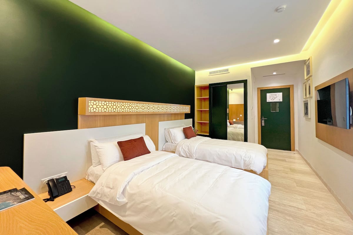 A hotel room with two beds, a desk with a phone, and a mirror.