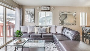 A living room with a leather sofa, a glass coffee table, and a view of a snowy landscape through large windows.